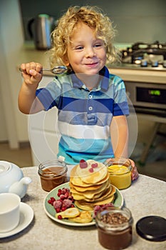 Little curly boy eating sweet pancakes
