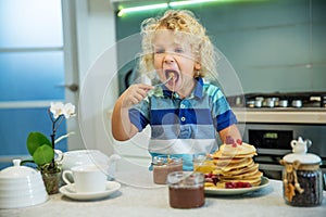 Little curly boy eating sweet pancakes