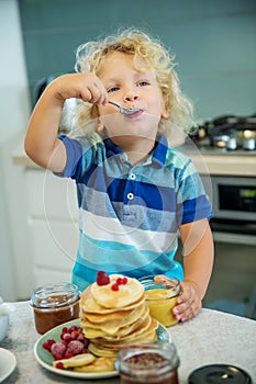 Little curly boy eating sweet pancakes