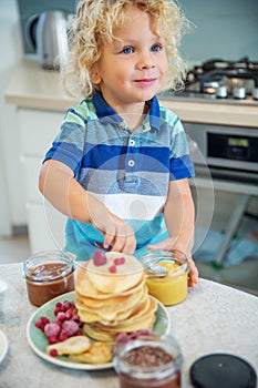 Little curly boy eating sweet pancakes