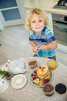 Little curly boy eating sweet pancakes