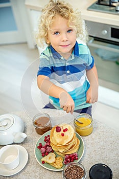 Little curly boy eating sweet pancakes