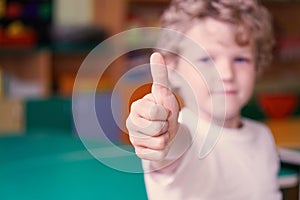 Little curly boy show his thumb up. Image with depth of field.