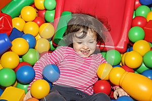 Little curly cute smile girl plays in balls for a dry pool. Play room. Happiness
