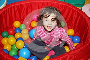 Little curly cute smile girl plays in balls for a dry pool. Play room. Happiness