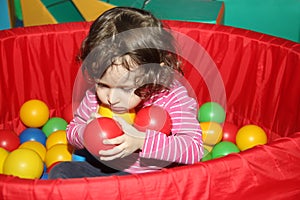 Little curly cute smile girl plays in balls for a dry pool. Play room. Happiness. the child has hands full of balls