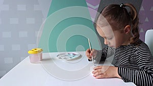 A little curly girl of European appearance of 3-4 years old paints a plaster figure of a hippo. Home hobby and fun game.