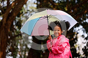 Little curly hair girl wearing raincoat colour pink good humour as she holds a umbrella