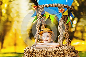 Little curly-haired boy in the air dreaming looks into the sky. Baby in a balloon basket