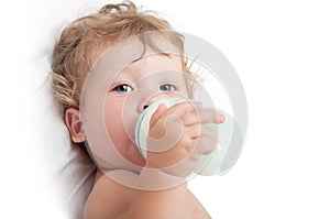 Little curly-headed baby sucks a bottle of milk