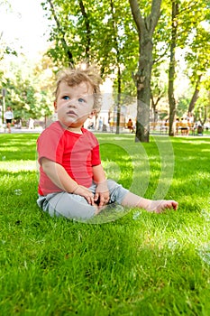 Little curly-headed child is sitting on the green grass