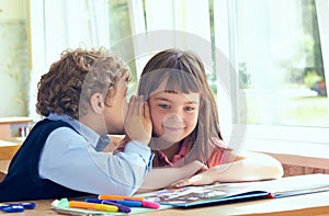 Little curly schoolboy whispering secrets during class at the elementary school