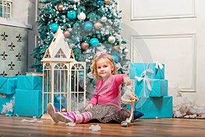 Little curly smiling girl sitting nearly Christmas tree