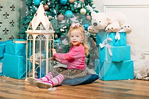 Little curly smiling girl sitting nearly Christmas tree