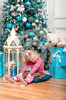 Little curly smiling girl sitting nearly Christmas tree