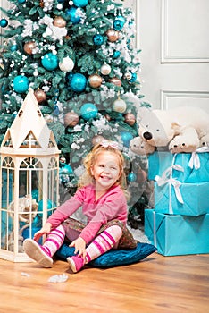 Little curly smiling girl sitting nearly Christmas tree