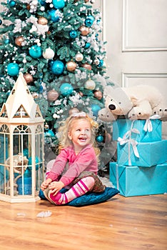 Little curly smiling girl sitting nearly Christmas tree