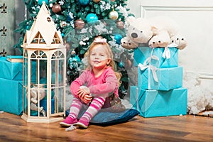 Little curly smiling girl standing nearly Christmas tree