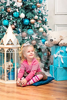 Little curly smiling girl standing nearly Christmas tree