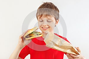 Little cut boy take out a big hamburger from a paper package on white background