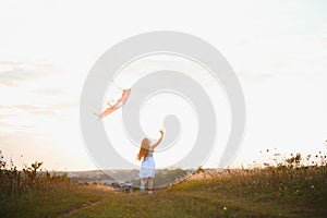 Little cute 7 years old girl running in the field with kite on summer day