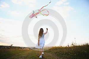 Little cute 7 years old girl running in the field with kite on summer day