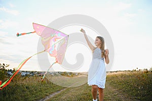 Little cute 7 years old girl running in the field with kite on summer day