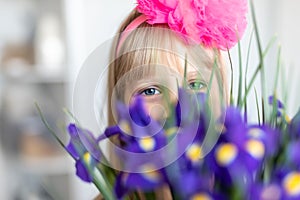 Little cute adorable blond caucasian female child girl portrait with beautiful blue eyes holding fresh purple iris