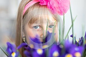 Little cute adorable blond caucasian female child girl portrait with beautiful blue eyes holding fresh purple iris flower bouquet