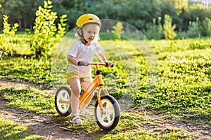 Little cute adorable caucasian toddler girl having fun riding exercise balance run bike push scooter in park forest.