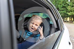 Little cute adorable happy caucasian toddler boy sitting in child safety seat car open window enjoy having fun making