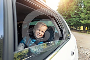 Little cute adorable happy caucasian toddler boy sitting in child safety seat car open window enjoy having fun making