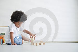Little cute African American boy sitting on the floor and playing toys holding wooden blocks at home