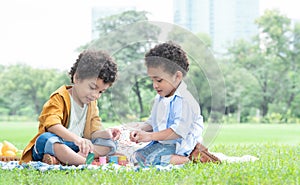 Little cute African American curly hair children boys sitting and have fun playing wooden blocks toy in green park together.