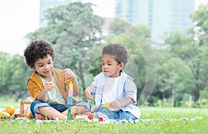 Little cute African American curly hair children boys sitting and have fun playing wooden blocks toy in green park together.