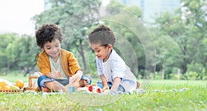 Little cute African American curly hair children boys sitting and have fun playing wooden blocks toy in green park together.