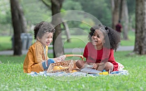 Little cute African children boy and girl sitting laughing and have fun playing magnifying glass while picnic at park together.