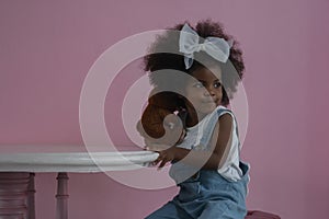 Little cute African girl smile and holding teddy bear in her hand sitting on a chair