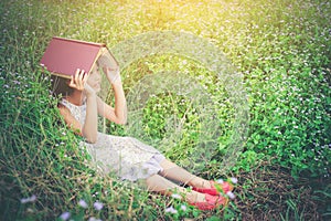 Little cute asian girl cover book on her head at nature.