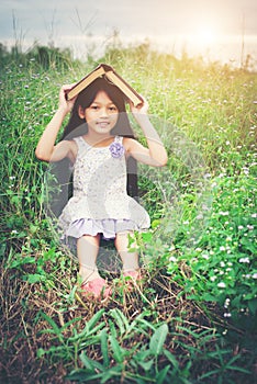 Little cute asian girl cover book on her head at nature.