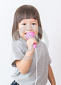 Little cute asian girl singing holding microphone over white background.