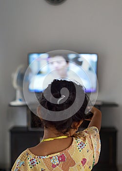Little cute asian girl watching tv and pointing remote to control television at home