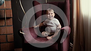 Little cute baby boy climbs on his own on beautiful armchair in slow motion