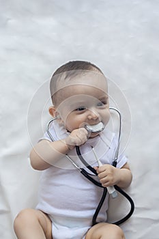 Little cute baby doctor. 6-month old baby boy playing with stethoscope. Kid having fun like a doctor