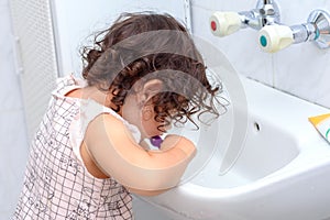 Little cute baby girl cleaning her teeth with toothbrush in the bathroom.