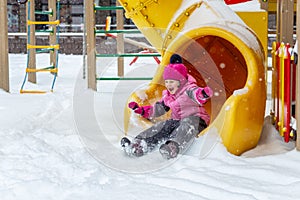 Little cute baby girl having fun on playground at winter. Children winter sport and leisure outdoor activities