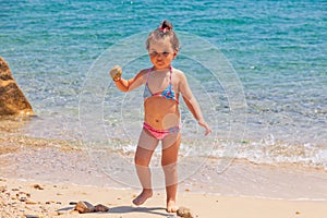 A little cute baby girl is playing on a beach near a sea