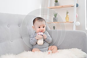 Little cute baby girl sitting in room on sofa drinking milk from