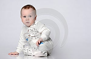 Little cute baby sitting on the floor in the studio in a summer cotton suit, in a cotton suit on a light background