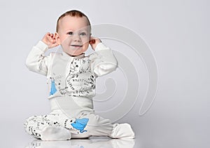 Little cute baby sitting on the floor in the studio in a summer cotton suit, in a cotton suit on a light background